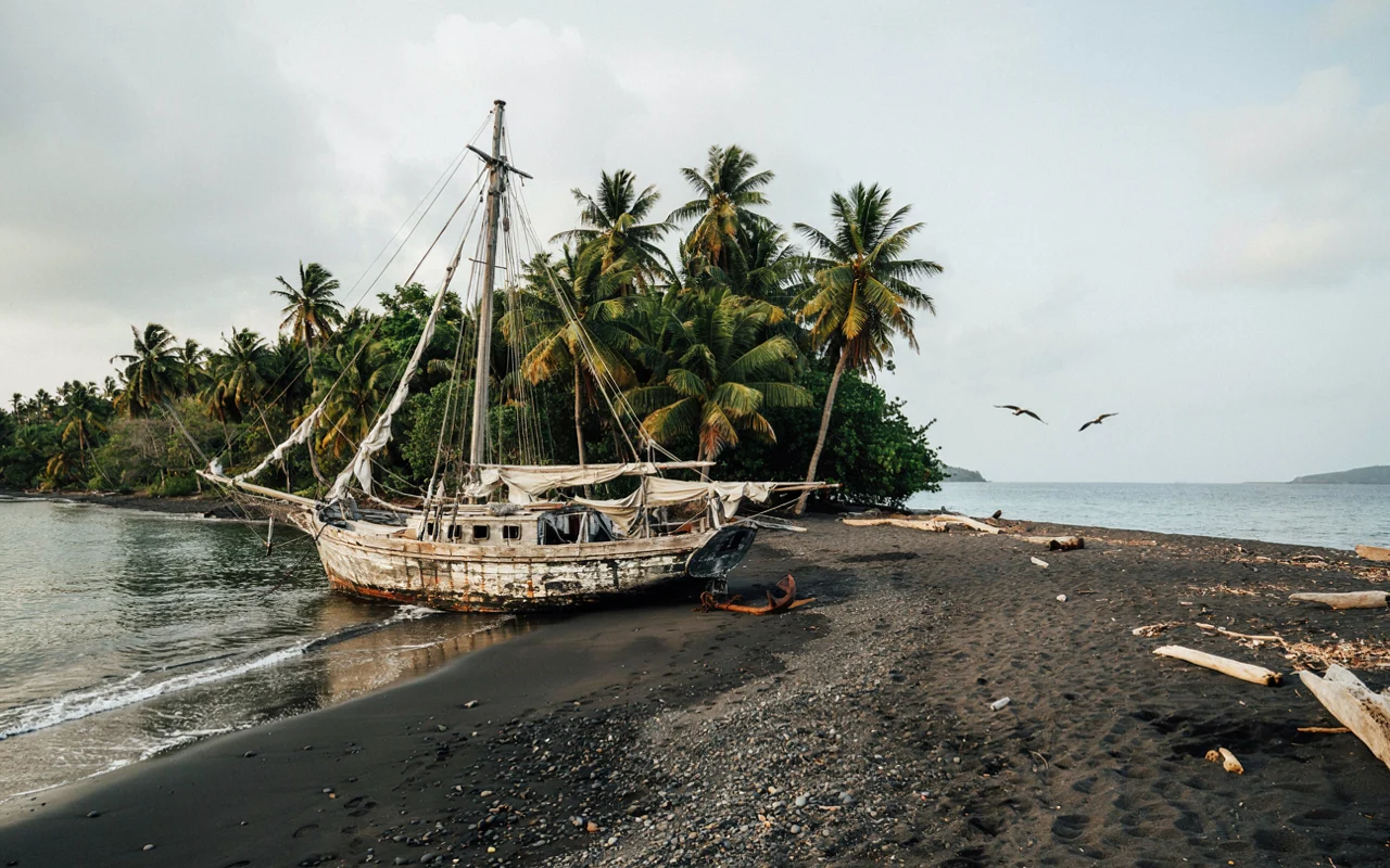 Un vieux navire amarré sur une plage sombre avec des palmiers en arrière-plan