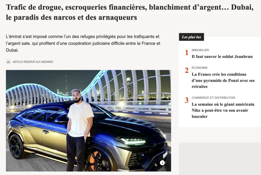 Un homme en chemise blanche se tient debout devant une automobile noire et or de grande taille sur un quai urbain.