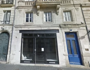 Façade de pierre calcaire avec une baie vitrée noire et une porte bleue.
