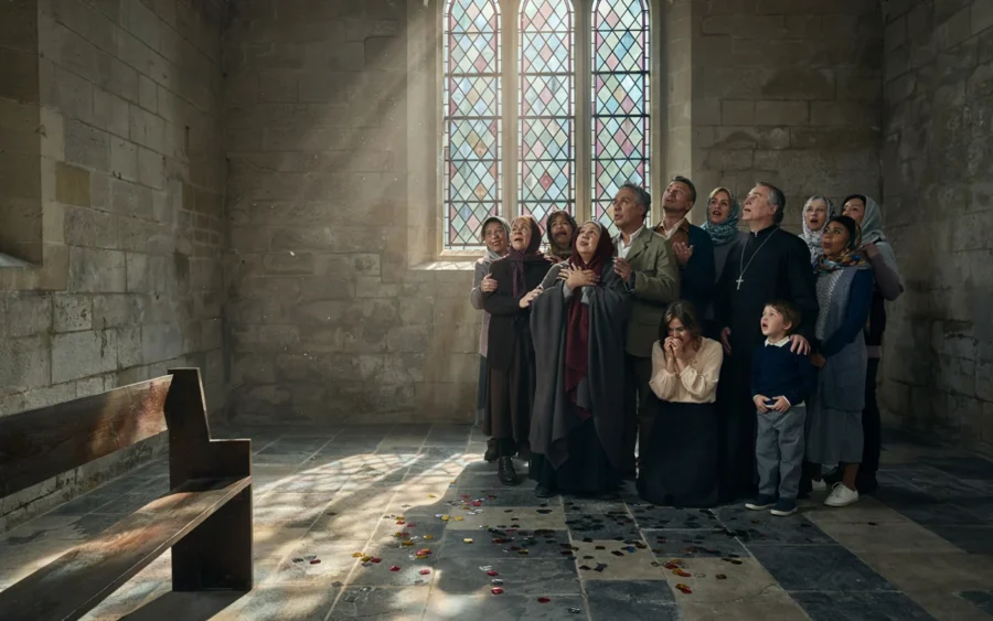 Groupe d'adultes et d'enfants rassemblés dans une église en pierre près d'une fenêtre en verre coloré.