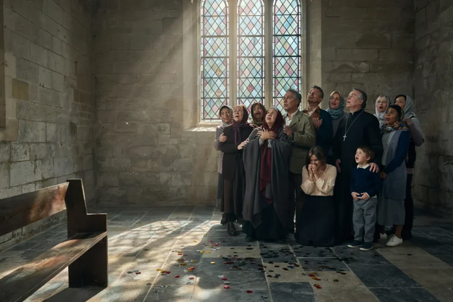 Groupe d'adultes et d'enfants rassemblés dans une église en pierre près d'une fenêtre en verre coloré.