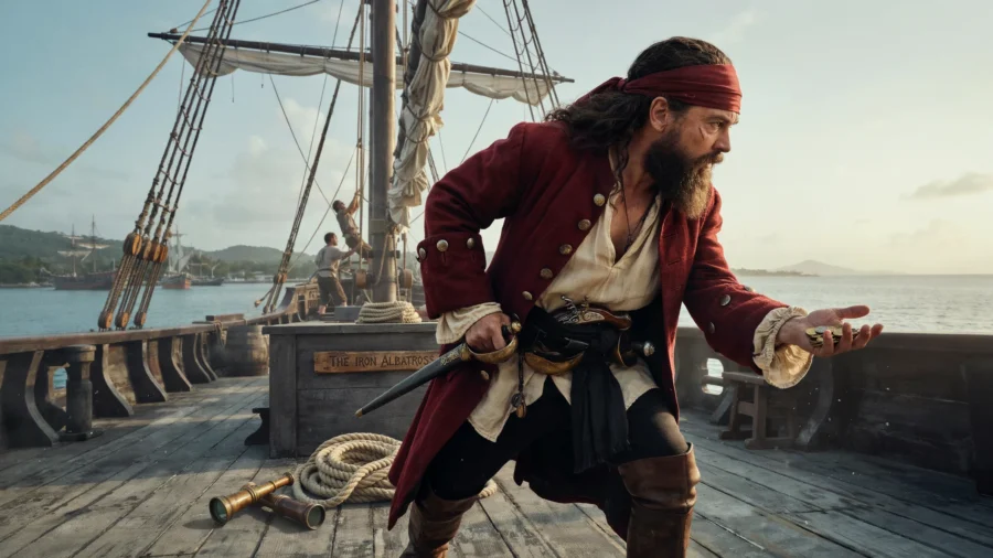 Un homme déguisé en pirate avec un bandeau rouge et un costume d'époque se tient sur le pont d'un bateau ancien.