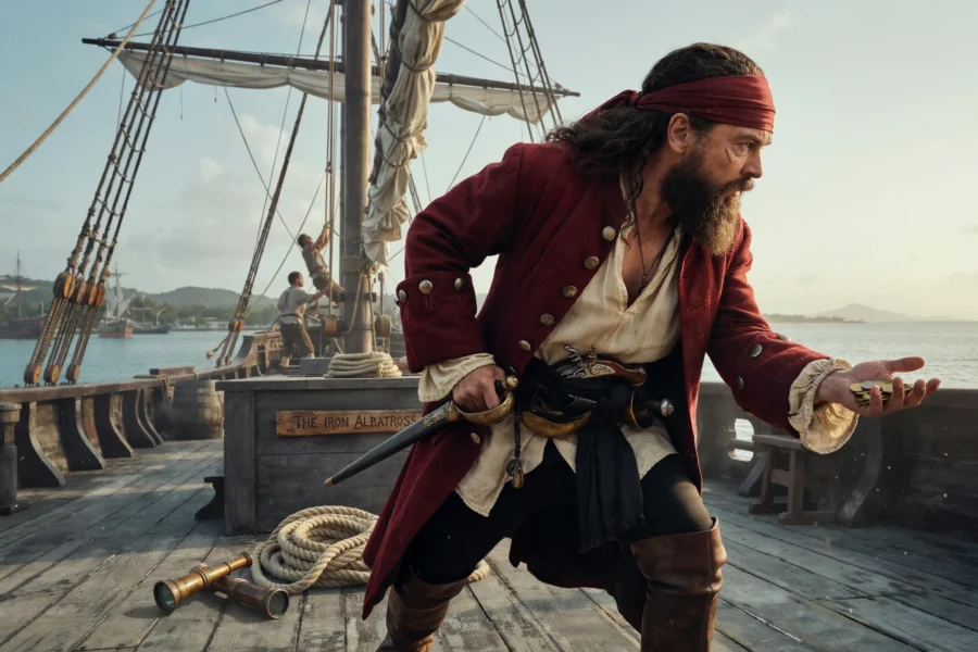 Un homme déguisé en pirate avec un bandeau rouge et un costume d'époque se tient sur le pont d'un bateau ancien.